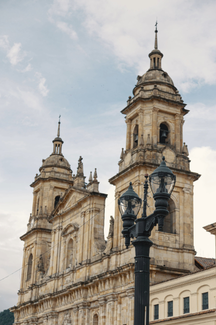 Catedral Primada vista lateral de la parte alta y sus torres con campanas. Con cielo azul grisaceo sobresale un farol negro antiguo con dos farolas de luces.