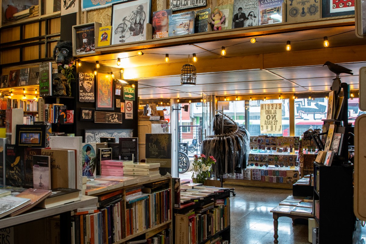La Valija de Fuego interior del local con estanterías repletas de libros, incluso en las paredes, y un exhibidor de ropa, parches y objetos decorativos. Hacia afuera se ve la calle con luz de día.