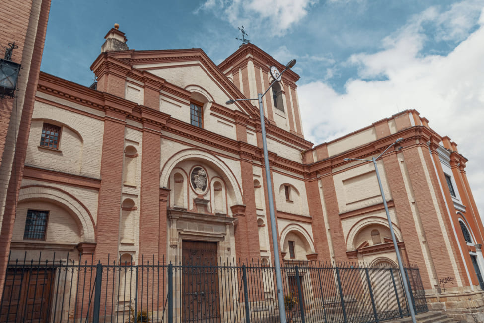  Iglesia San Ignacio de Loyola, fachada completa en la drillo y pintura amarilla en la que se ven ocho ventanas y cuatro puertas. En la torre más alta se observa el reloj.