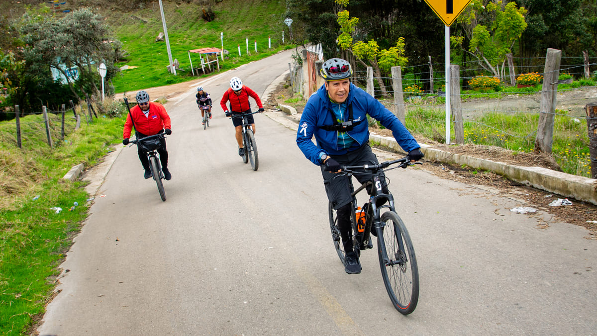 Ciclistas pedaléan con esfuerzo en subida por entre caminos rurales.