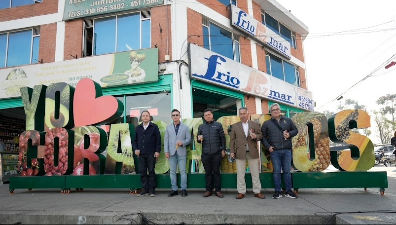 Grupo de hombres adultos parados al frente de un aviso gigante que dice "Yo amo Corabastos". Todos están con una copa en la mano.