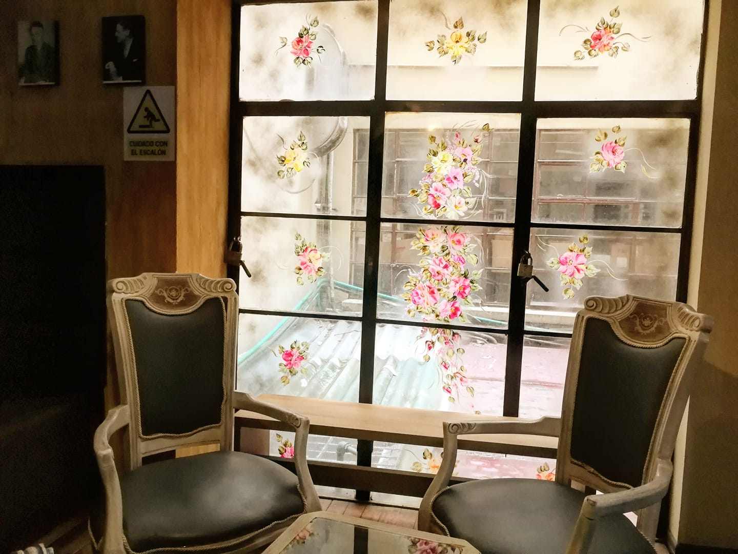 Salón interior con dos sillas antiguas y en buen estado y un ventanal de fondo con dibujos de rosas de colores.