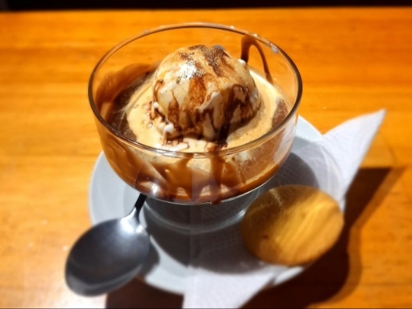 Una copa de helado con café, una galleta dorada y una cucharita, sobre un plato redondo.