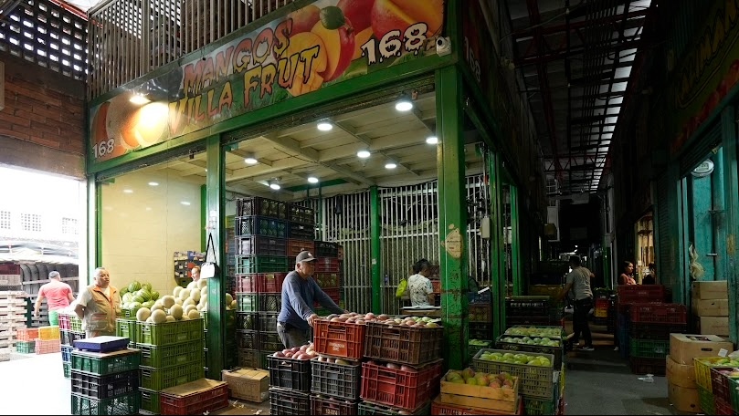 Interior de una plaza de mercado en la que se ve un local con muchas canastas con diferentes frutas.