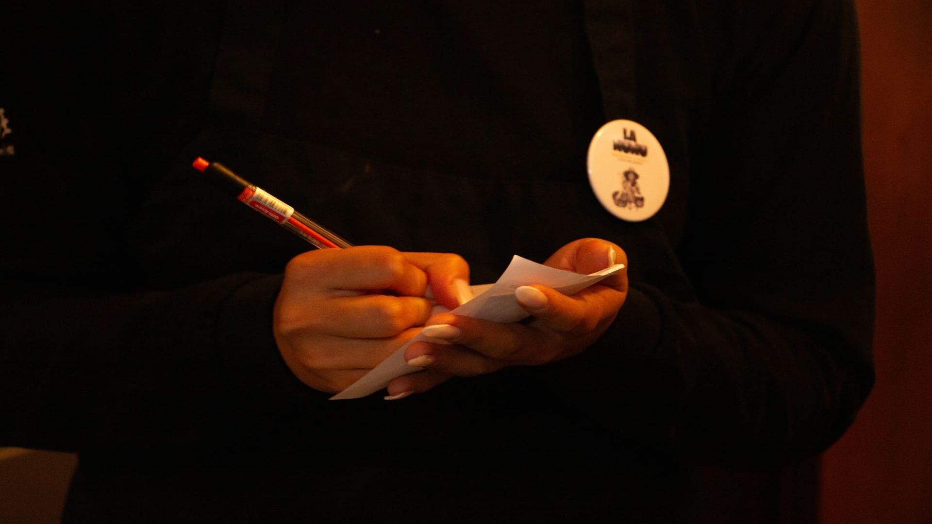 Primer plano de unas manos con manicura, escribiendo una orden en una libreta con un bolígrafo rojo.