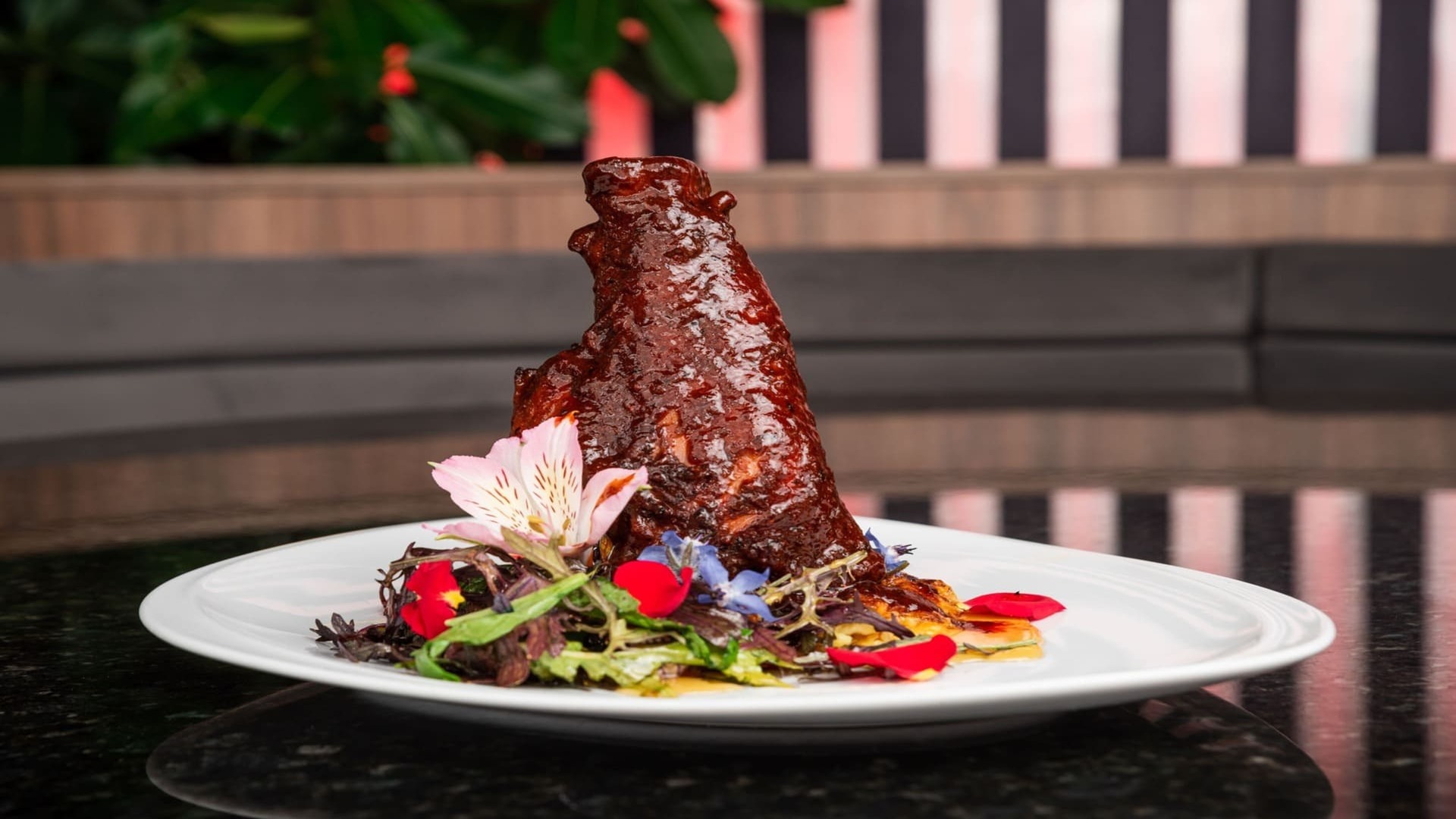 Costillas glaseadas y brillantes, bellamente emplatadas con una ensalada fresca y flores comestibles.