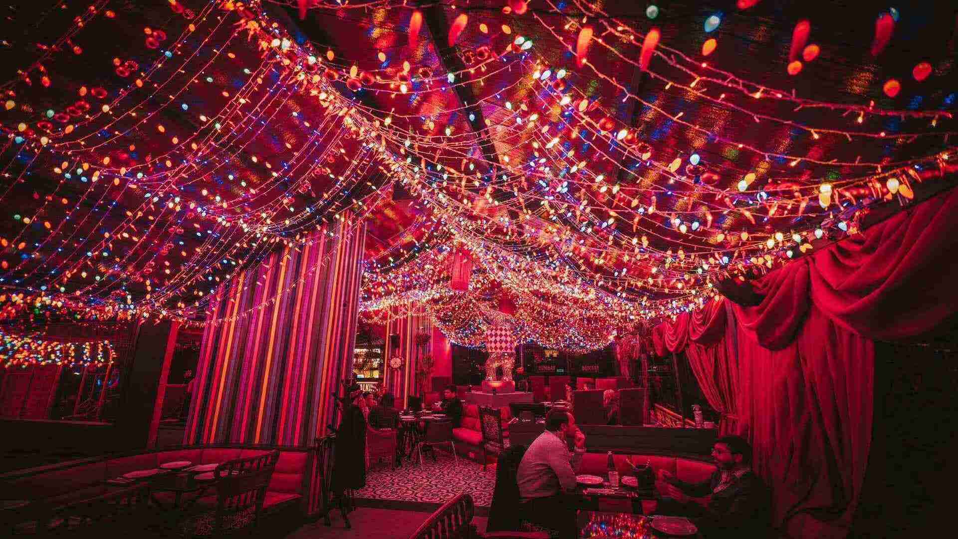 Un restaurante o bar con luces navideñas multicolores que cubren el techo y decoraciones rojas vibrantes.