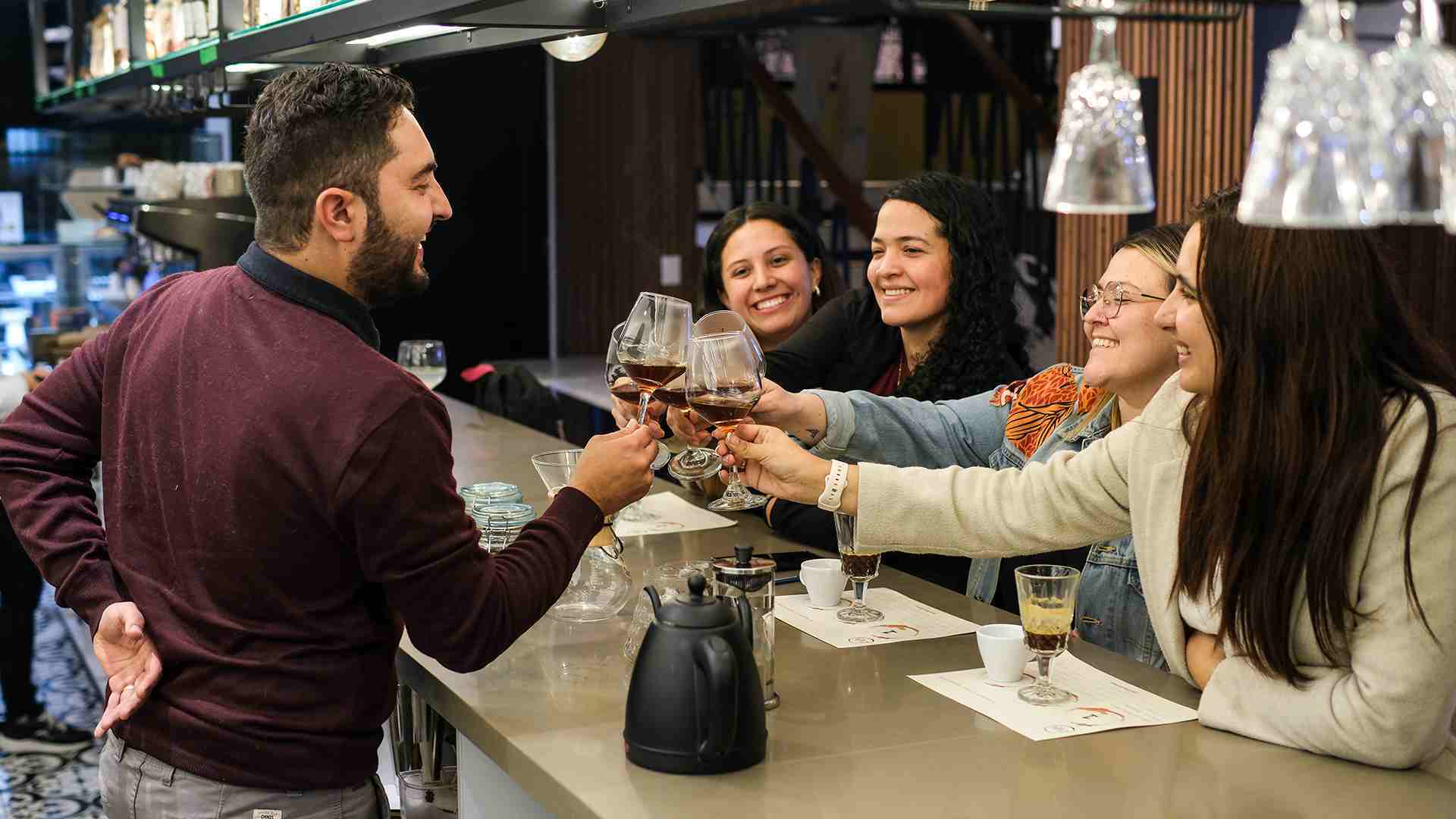 Un grupo de amigos sonrientes brinda con copas de vino o café en una barra de Caffa.