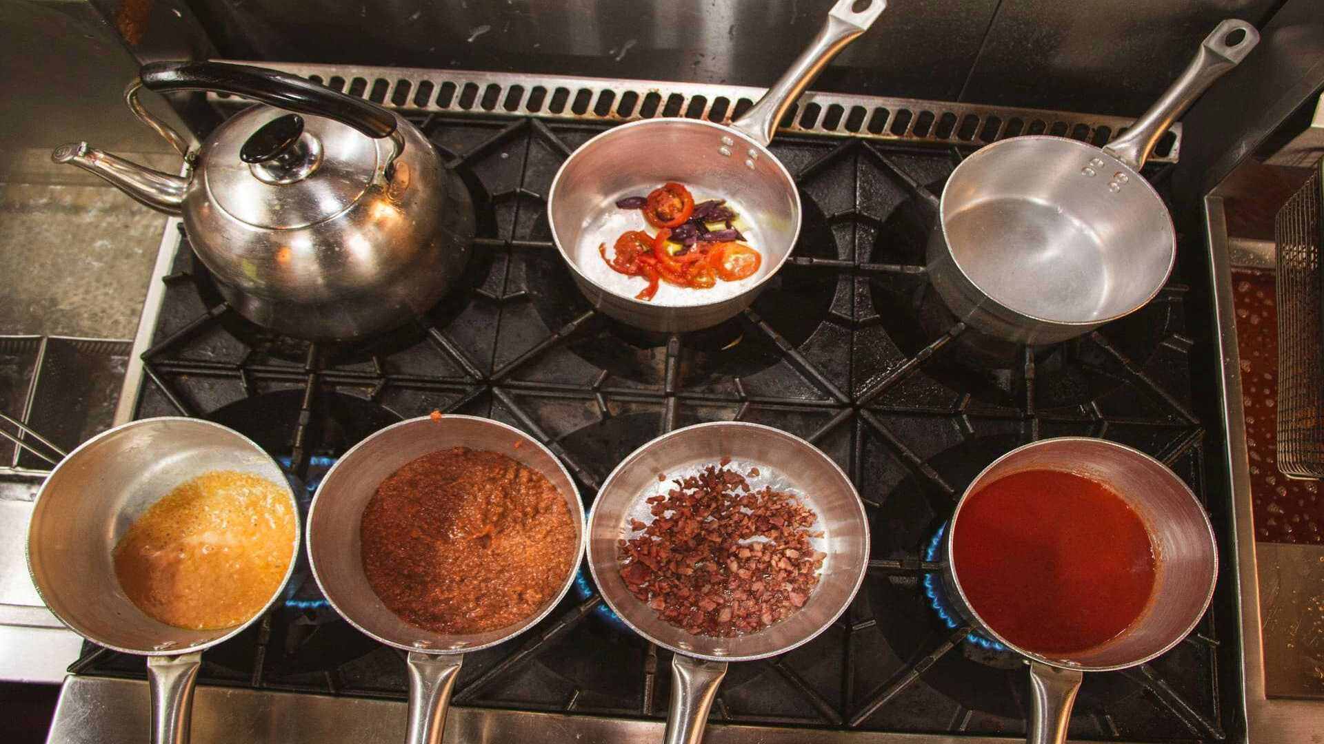 Varias ollas pequeñas con diferentes ingredientes y salsas cocinándose en una estufa de cocina.