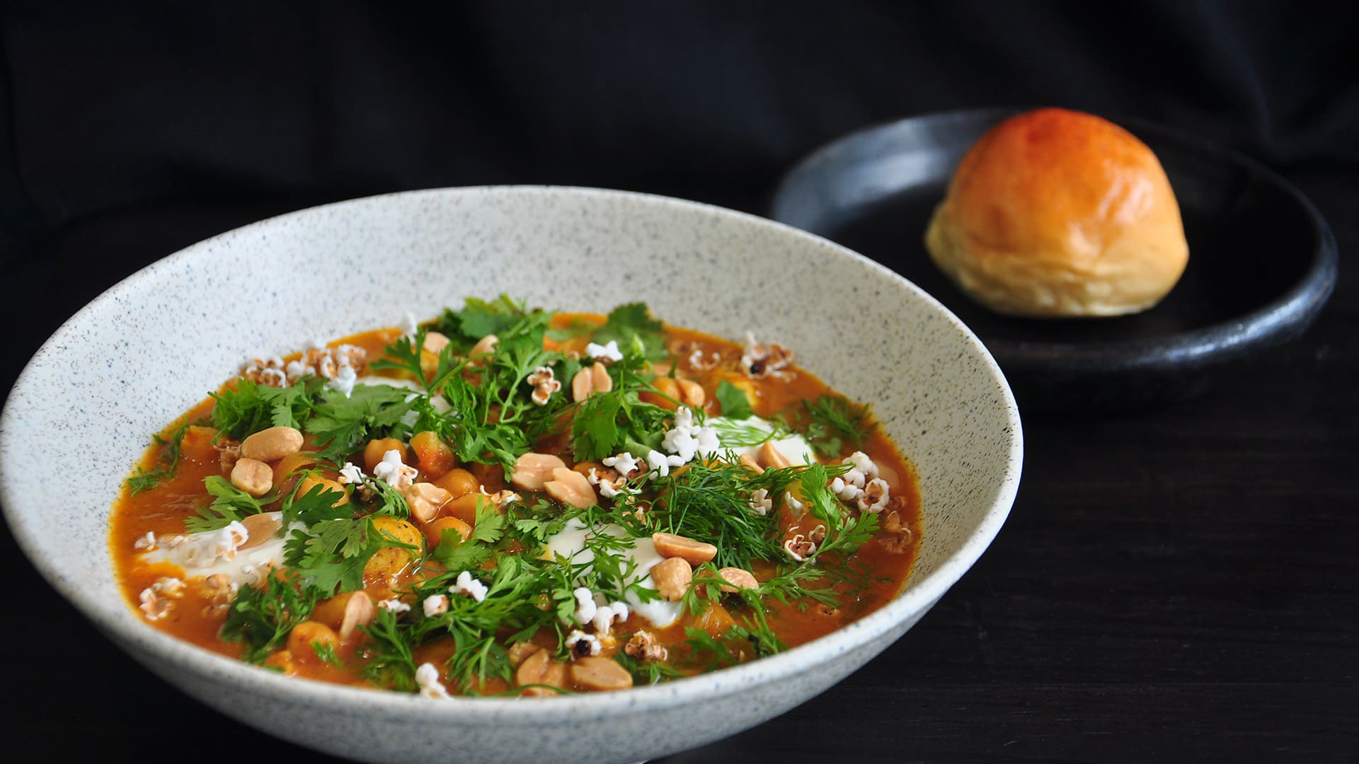 Un tazón de sopa o estofado con garbanzos, cilantro, eneldo y palomitas de maíz, servido con un pan.