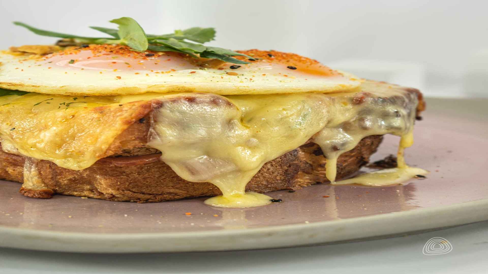 Un sándwich Croque Madame con mucho queso fundido, jamón y un huevo frito en la parte superior.