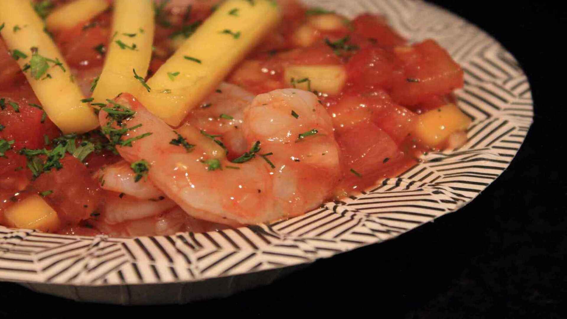 Ceviche de camarón con trozos de tomate y mango, realzado con finas hierbas, en un plato decorativo.