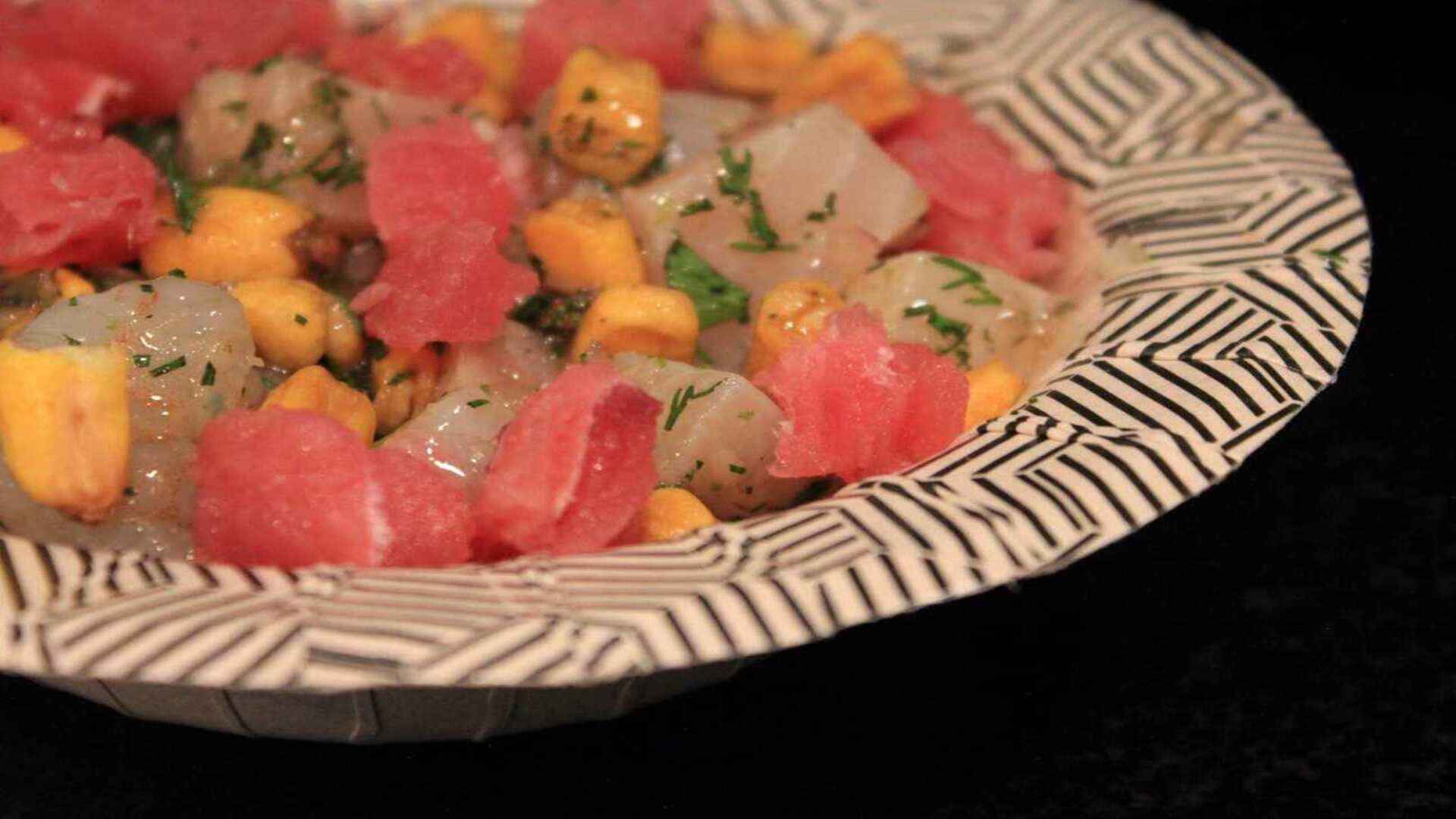 Ceviche con cubos de sandía, mango y pescado, adornado con perejil fresco en un plato blanco y negro.