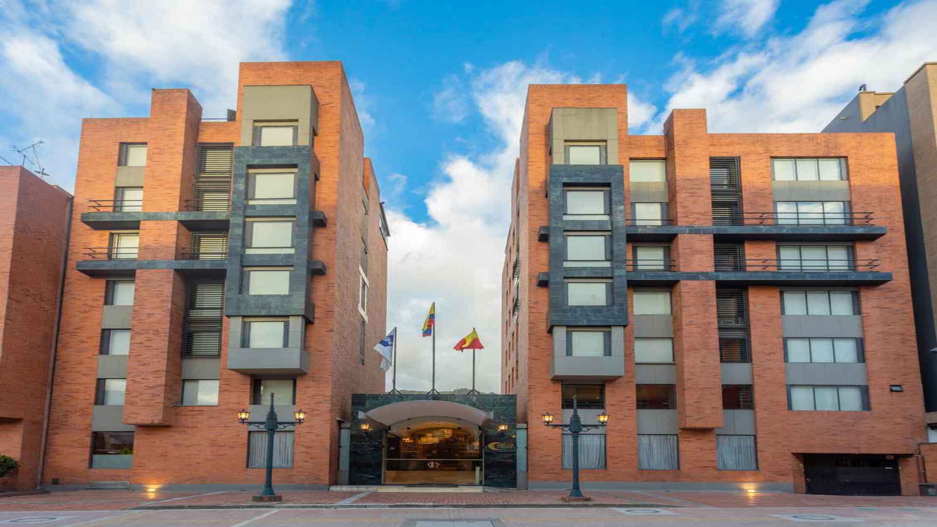 Fachada moderna de un hotel de ladrillo rojo con dos torres y entrada principal. 