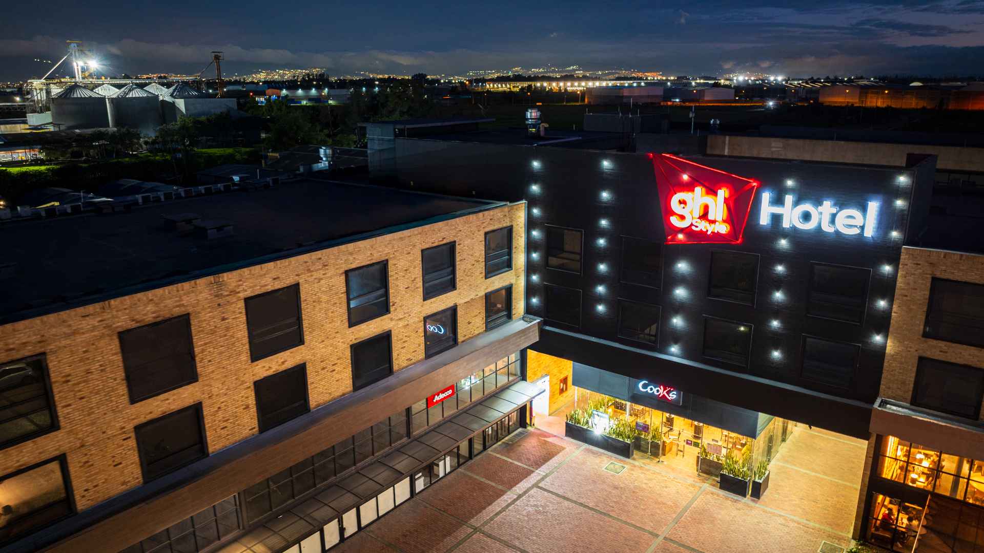 Vista aérea nocturna del hotel Style con edificios circundantes y luces urbanas.
