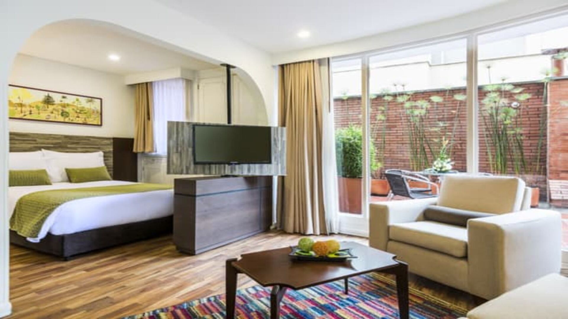 Esta imagen muestra una suite de hotel espaciosa y bien iluminada, con una sala de estar cómoda y un área de comedor, conectada a un dormitorio. La decoración es moderna y funcional.