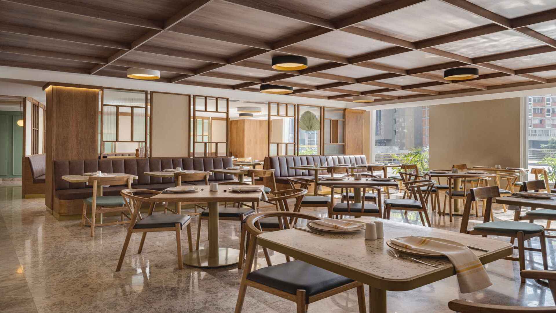 Restaurante luminoso con mesas de madera, asientos cómodos y techo enrejado.