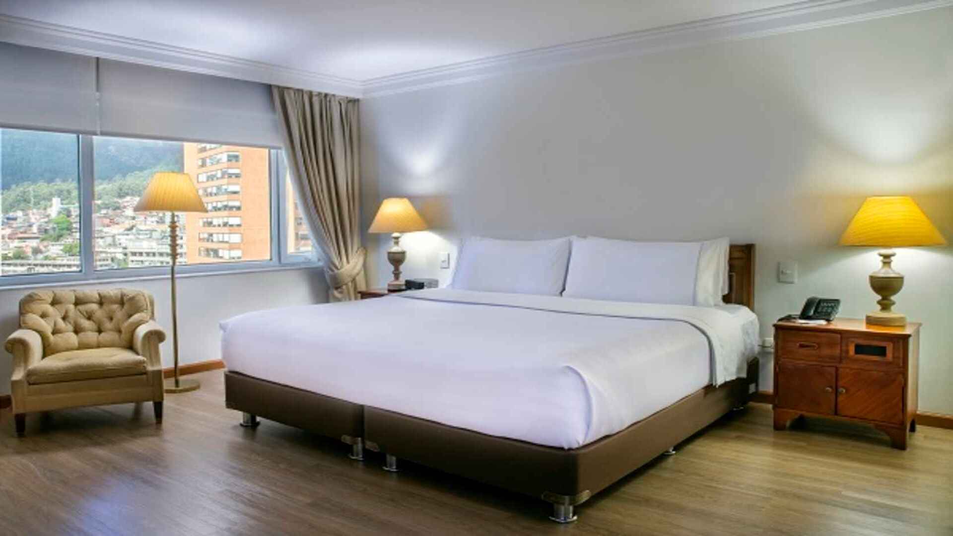 Habitación de hotel con cama king-size y sillón. Espaciosa y luminosa, con mobiliario clásico.
