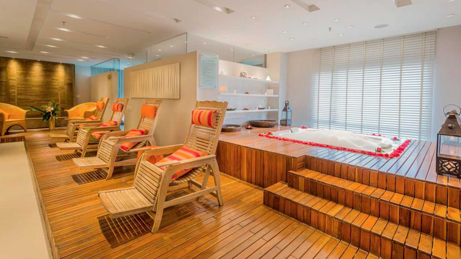 Spa: Spa cálido en madera con jacuzzi elevado, sillas de descanso acolchadas y luz relajante. Aromas, velas y pétalos rojos.