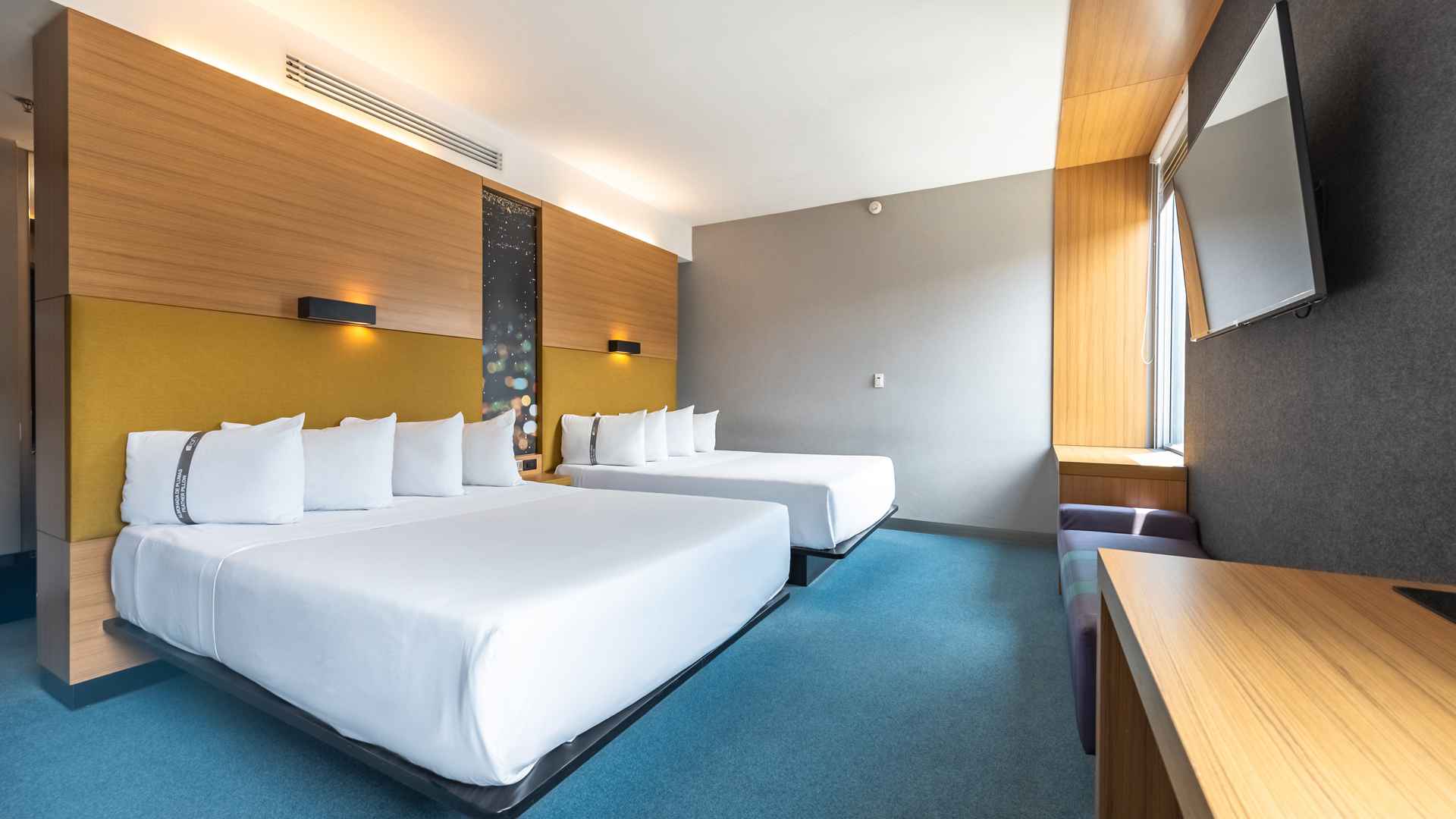  Una habitación de hotel Aloft con dos camas dobles, un banco junto a la ventana y una decoración moderna y colorida, ideal para familias o grupos.