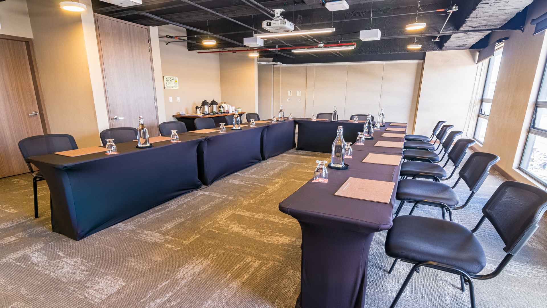 Sala de reuniones configurada en forma de U con mesas y sillas negras.