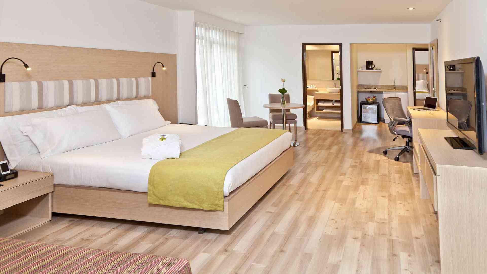 Una espaciosa habitación de hotel con una cama grande, una pequeña mesa de comedor, escritorio y una cocina americana con mini-nevera y cafetera.