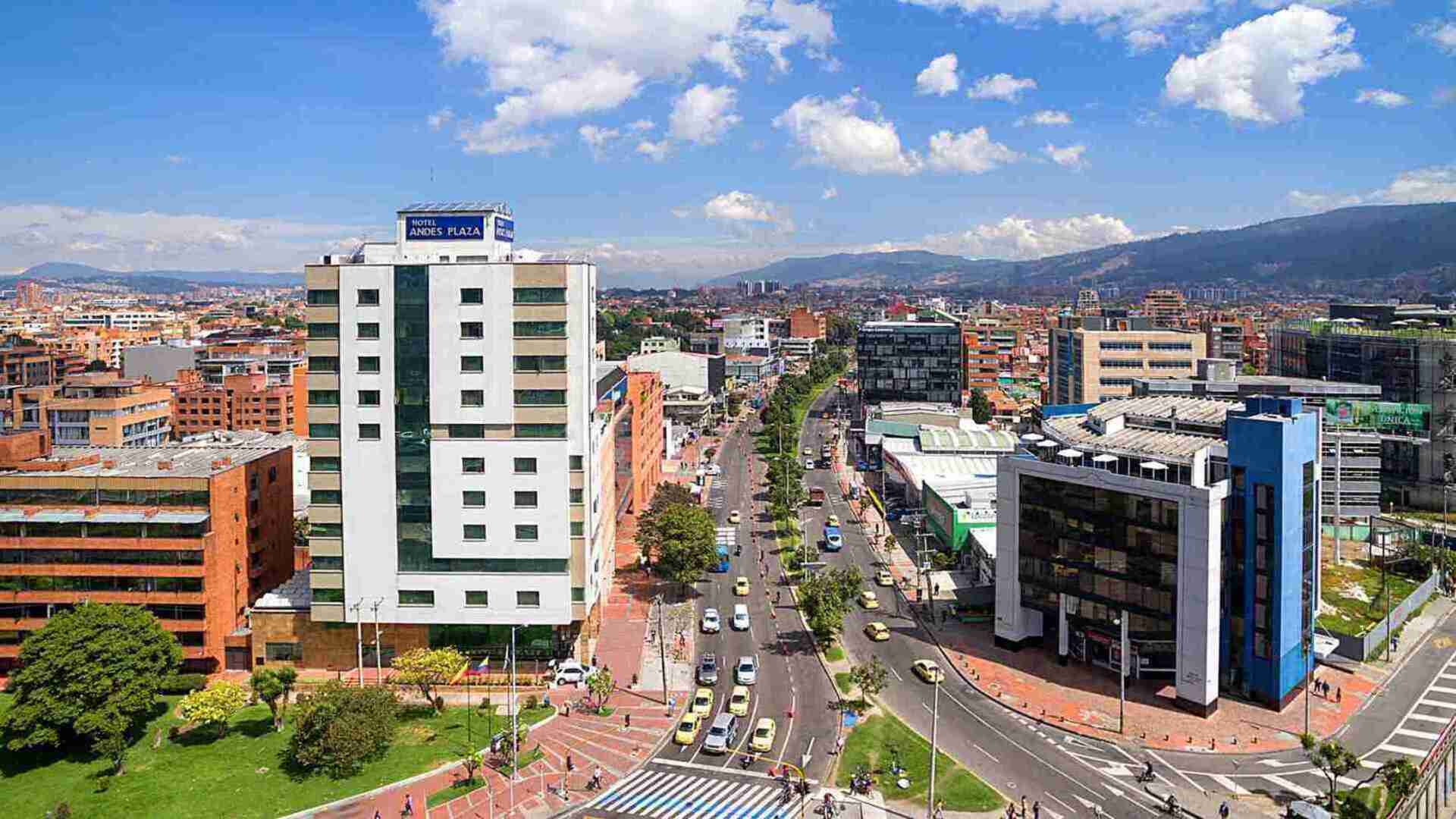 Una vista aérea de una bulliciosa calle de la ciudad con edificios modernos y montañas al fondo. El "Hotel Andes Plaza" se destaca en el paisaje urbano.