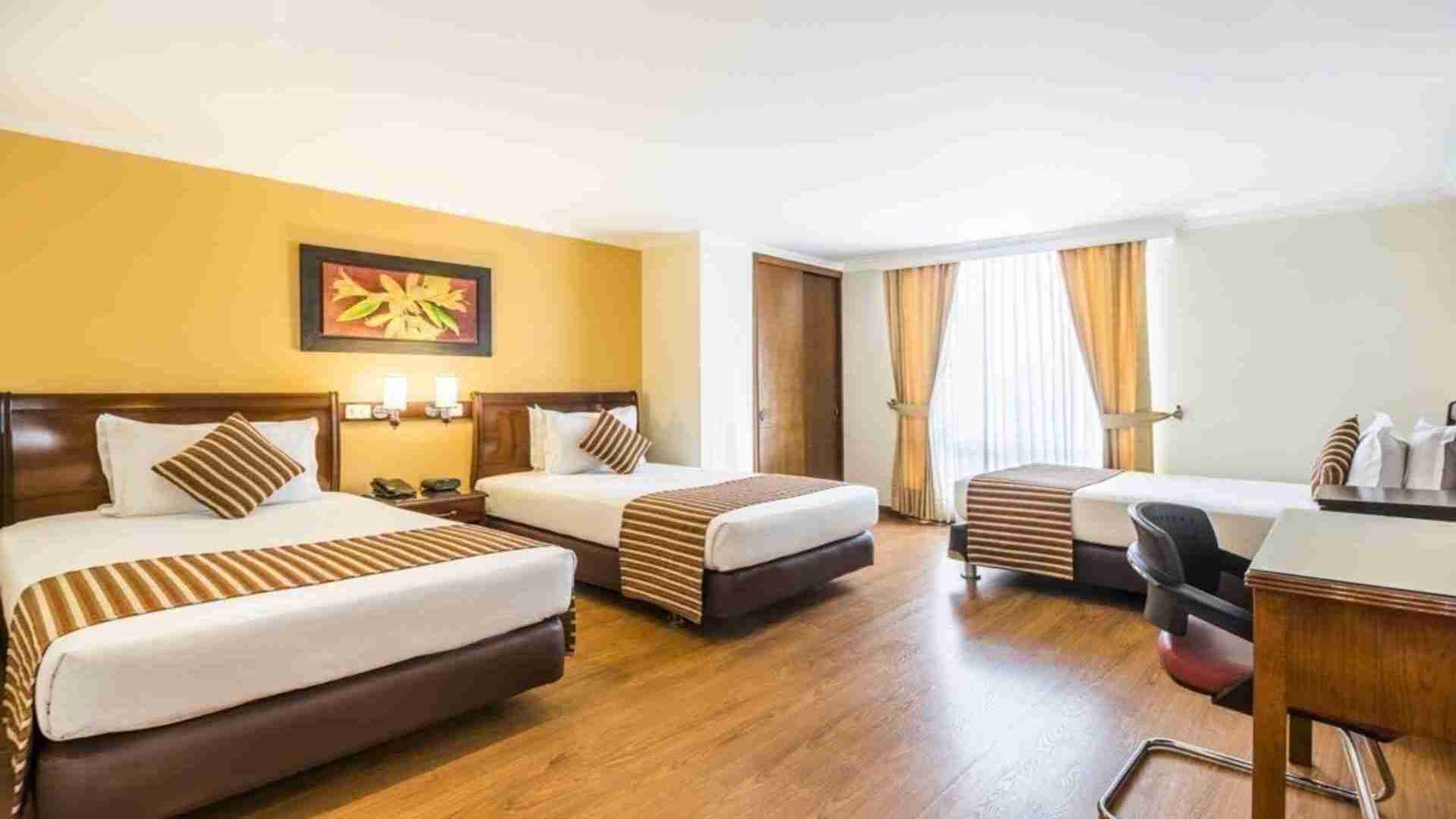 Un dormitorio triple de hotel con tres camas individuales, ideal para grupos o familias. La habitación cuenta con escritorio y un diseño funcional en tonos cálidos.