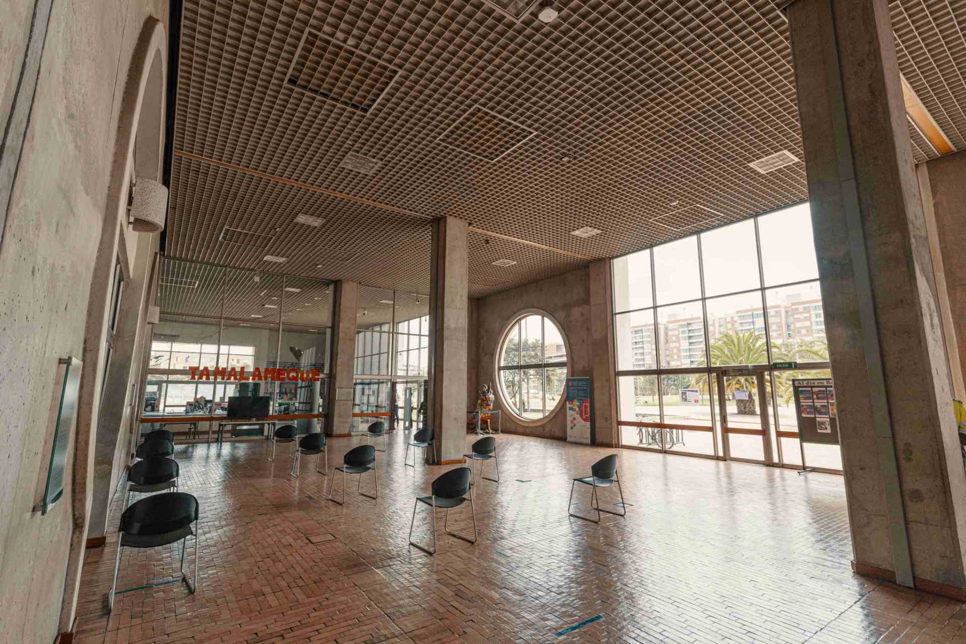 Biblioteca El Tintal al interior grandes paredes en concreto, techos en cuadros de madera y ventanales gigantes circulares y cuadrados.