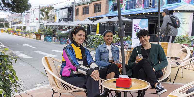 Distrito San Felipe, personas departiendo, tomando sentados en sillas de mimbre. Detras se ven las fachadas de varios negocios comerciales.